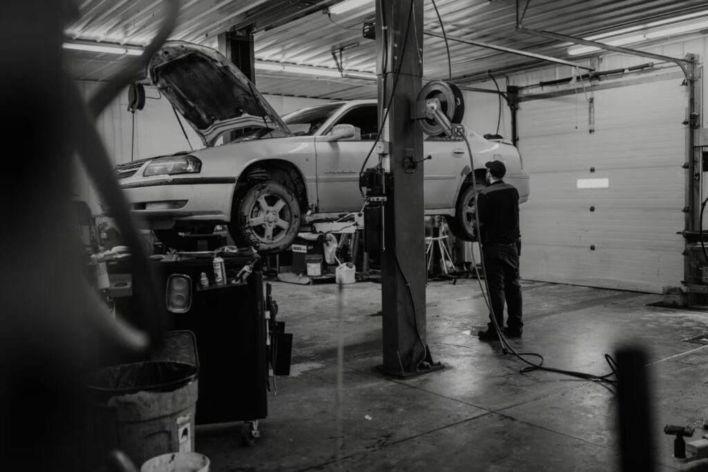 Auto mechanic inspecting a raised car in a repair shop with the hood open.
