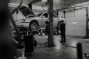Auto mechanic inspecting a raised car in a repair shop with the hood open.