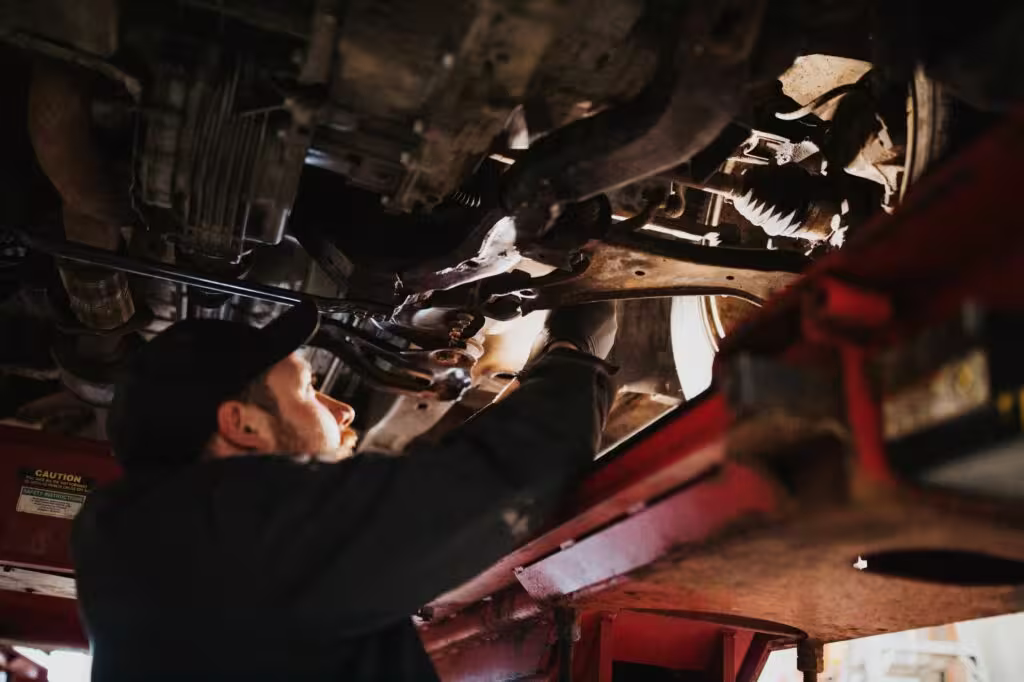 Mechanic working under a lifted car, tightening bolts on the suspension system.