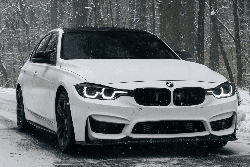 European auto repair in Long Lake, MN at Arvu Auto. Image of a white BMW driving on a snow-covered road, highlighting seasonal maintenance for safe, reliable cold-weather performance.