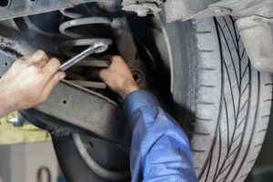 Auto technician using a wrench to adjust a car's rear suspension components.