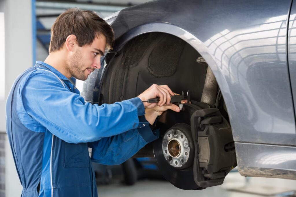 Mechanic in blue overalls measuring a car brake disc with a caliper.