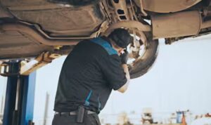 Mechanic working underneath a lifted car, inspecting the rear wheel assembly.