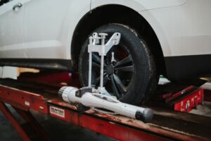 A white car on a red automotive lift with a wheel alignment tool attached to the rear tire.