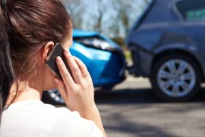 Woman on the phone with two damaged cars in the background after a rear-end collision.