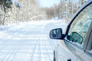 Side view of a car driving on a snow-covered road surrounded by a winter forest.