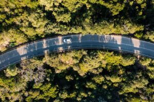 Aerial view of a car driving on a curved road surrounded by dense green forest.