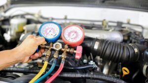 A mechanic's hand adjusting AC pressure gauges under a car hood.
