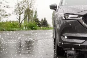 A close-up of a dark-colored car in the rain, with raindrops bouncing off the wet pavement.