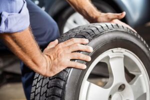 Close-up of a man's hands gripping a car tire, with a vehicle in the background.