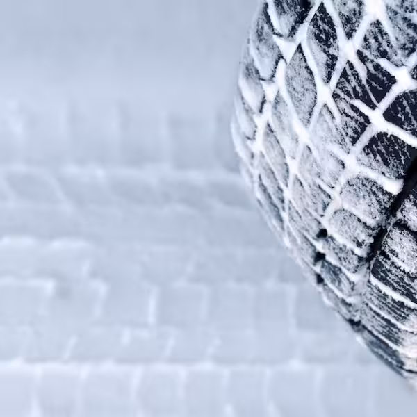 A winter tire covered in snow, leaving a tread pattern on the icy surface below.