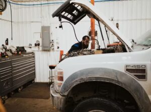 Mechanic working on a white Ford F-450 truck in a garage with tools and equipment in the background.
