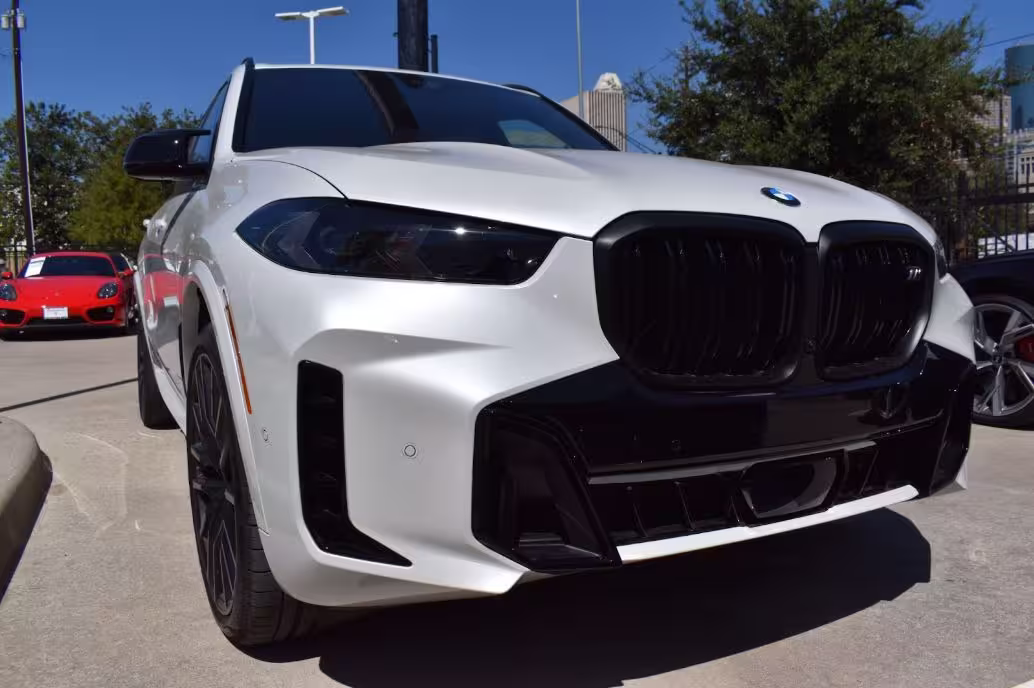 White BMW X5 M parked outdoors, featuring an aggressive black grille and sporty design.