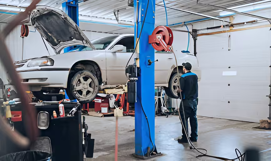 Auto technician inspecting a raised car in a garage with the hood open.