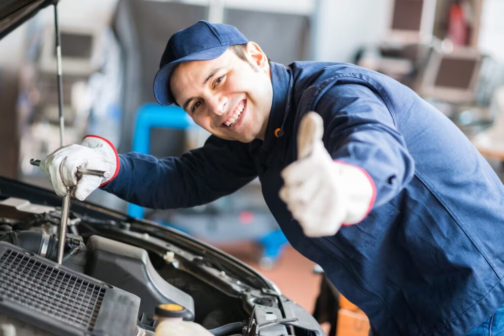 an auto mechanic, giving a thumbs-up while working on a car engine