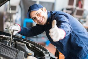 an auto mechanic, giving a thumbs-up while working on a car engine