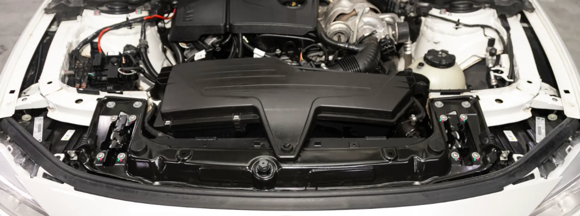 An overhead shot of a car's engine compartment, revealing the engine and its various components. The engine is centrally located and appears to be in good condition. The surrounding areas are clean and well-organized, with various wires, hoses, and other components visible. The lighting highlights the intricate details of the engine and its surroundings. The image suggests a focus on automotive engineering or maintenance.