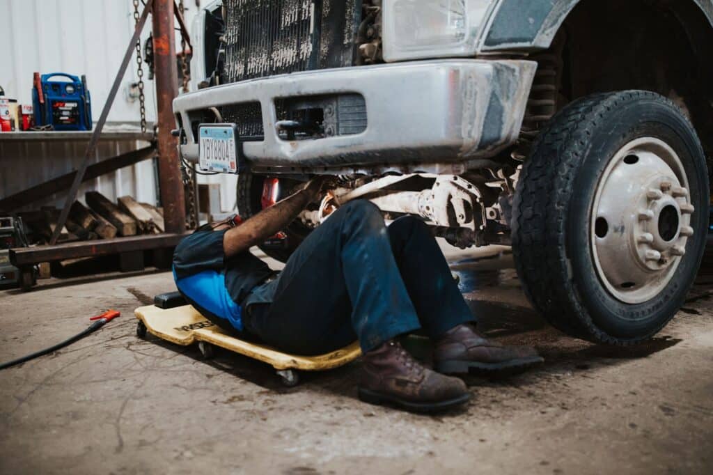 Mechanic working under a truck in a garage.