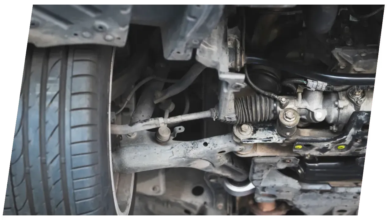 A close-up view from underneath a vehicle, showing the tire, suspension components, steering rack, and other parts of the undercarriage. The tire is a Bridgestone Potenza RE050A, visible on the sidewall. The various mechanical parts are interconnected and show signs of wear and use.