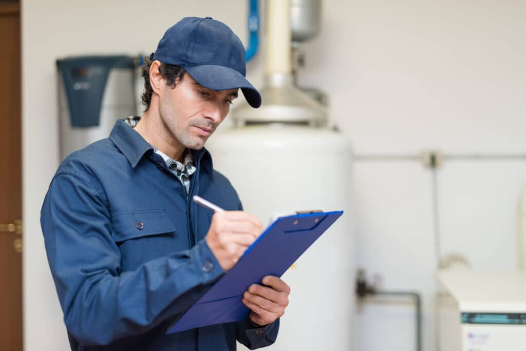 A person in a blue uniform writes on a clipboard indoors with industrial equipment in the background.