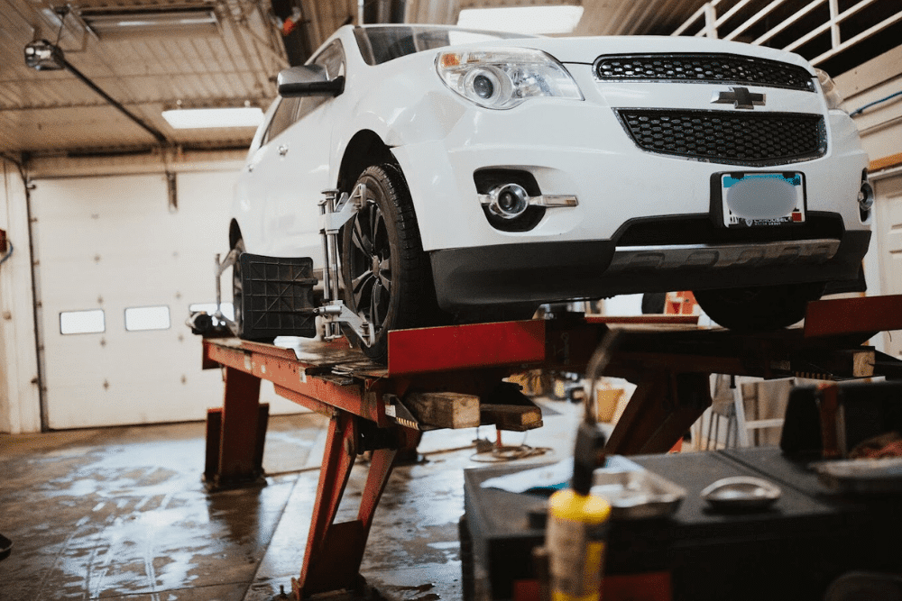 Auto repair near Annandale, MN by Arvu Auto. Image of a white Chevrolet SUV on a lift with alignment sensors attached to the wheels inside a well-lit service bay.