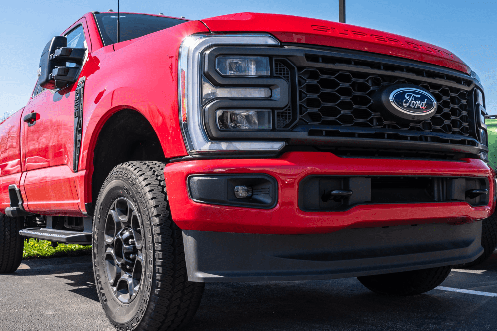 Ford problems, Ford repair in Long Lake, MN by Arvu Auto. Image of a red Ford Super Duty truck parked outdoors, showcasing its bold front grille, rugged tires, and powerful stance under clear blue skies.